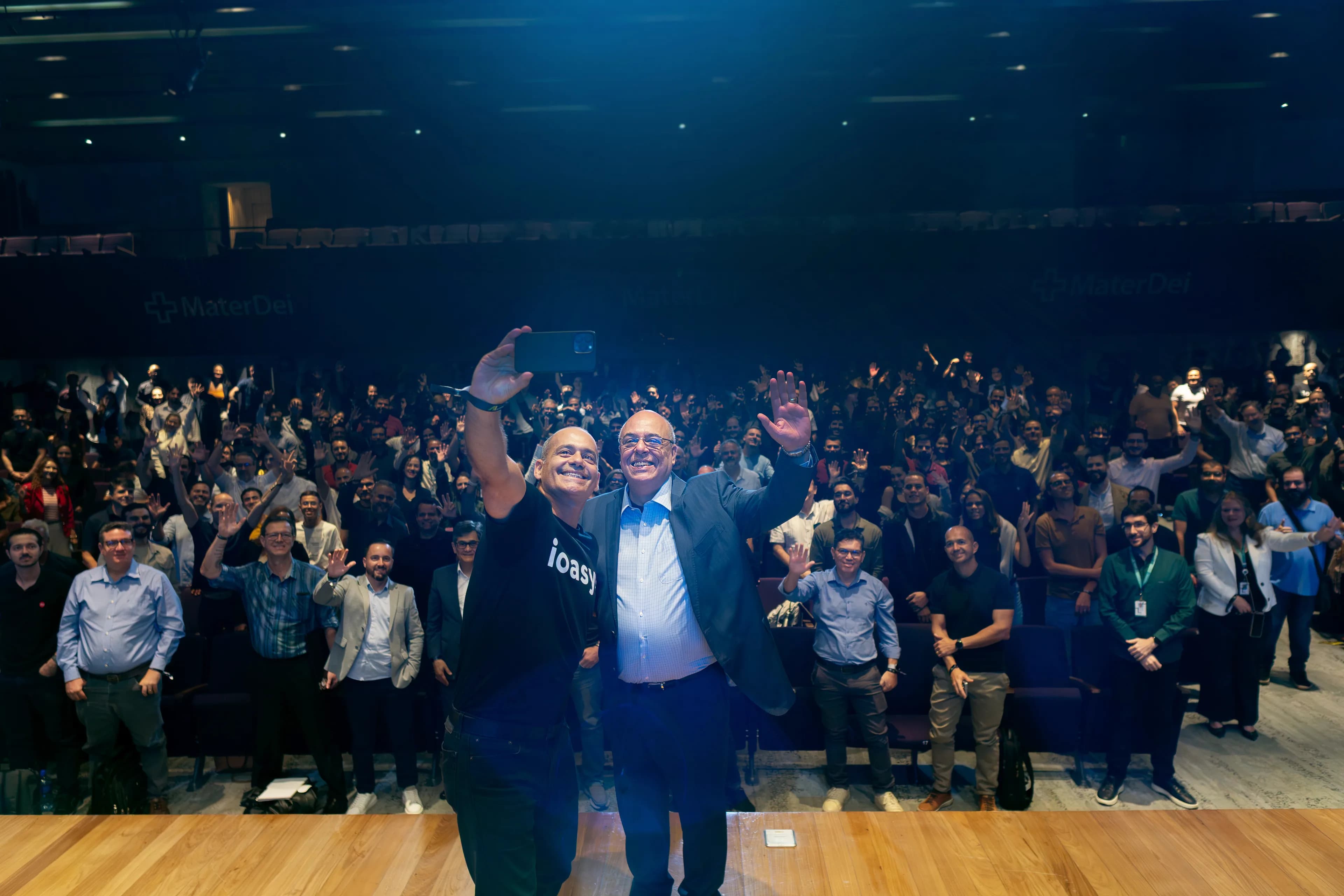 Organizadores do AI Summit tirando uma selfie com o auditório lotado ao fundo